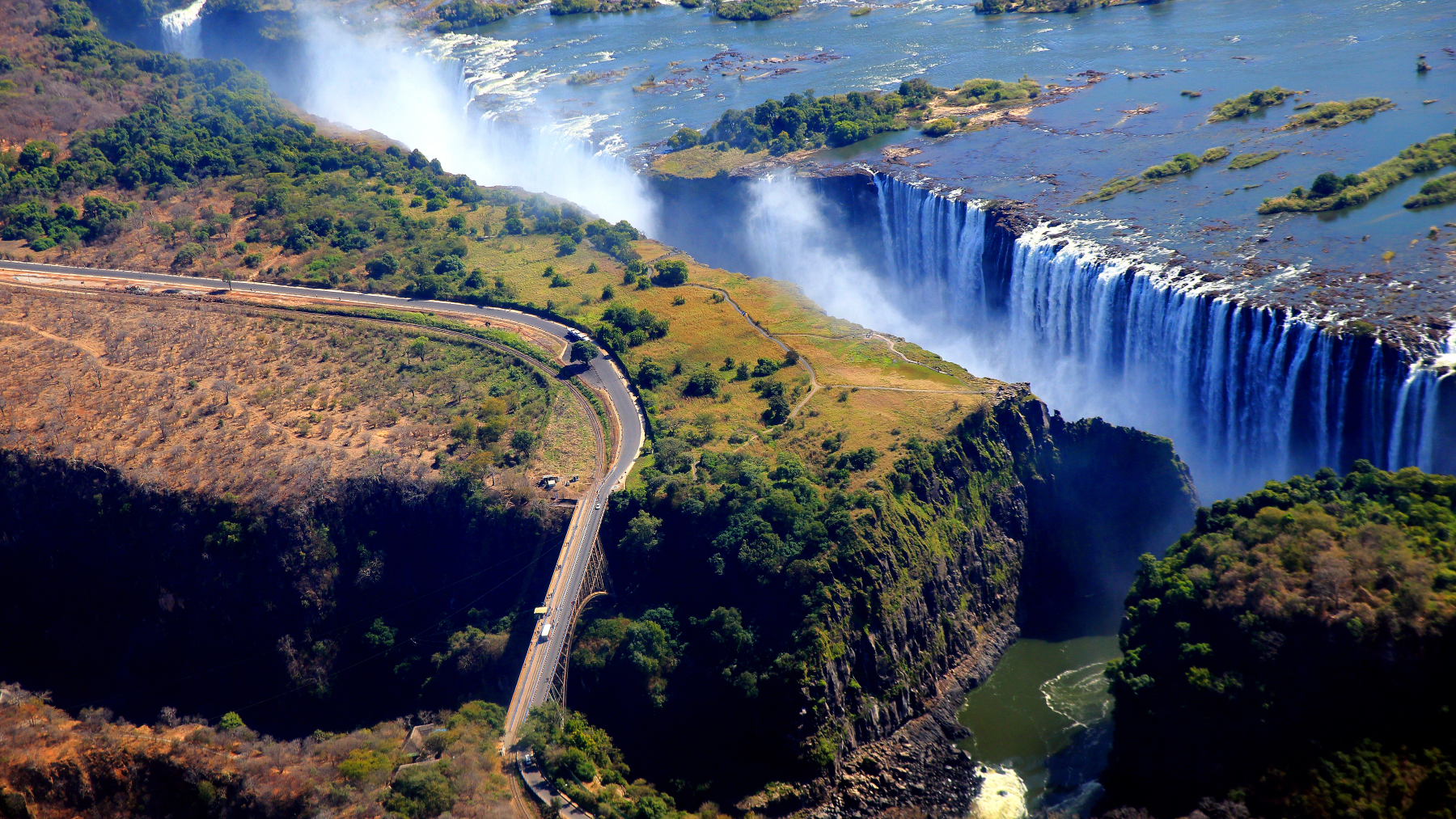 Vista aérea panorámica de las Cataratas Victoria y el puente fronterizo entre Zimbabue y Zambia, con el río Zambeze cayendo al abismo.