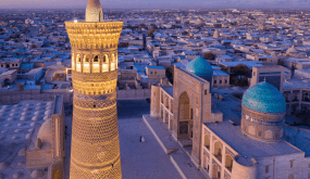 Vista Aérea Del Minarete Kalyan Iluminado Junto A Las Cúpulas Turquesas Del Complejo Po-i-Kalyan En Bujará, Uzbekistán, Al Atardecer