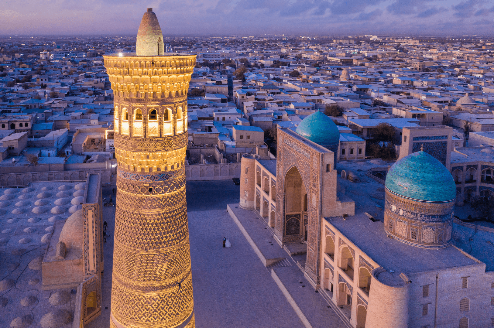 Vista aérea del minarete Kalyan iluminado junto a las cúpulas turquesas del complejo Po-i-Kalyan en Bujará, Uzbekistán, al atardecer